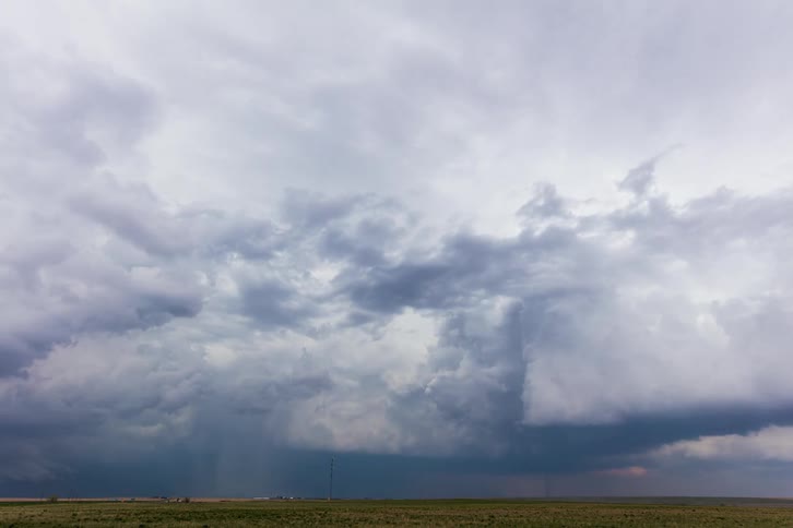 Dark storm clouds move over rural land and pour rain as traffic moves on the road