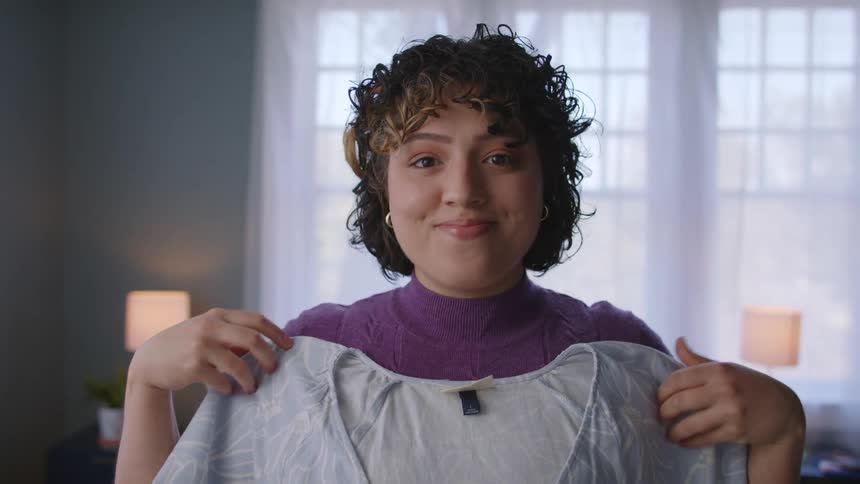 A woman putting blouses in front of her torso trying to pick one to wear
