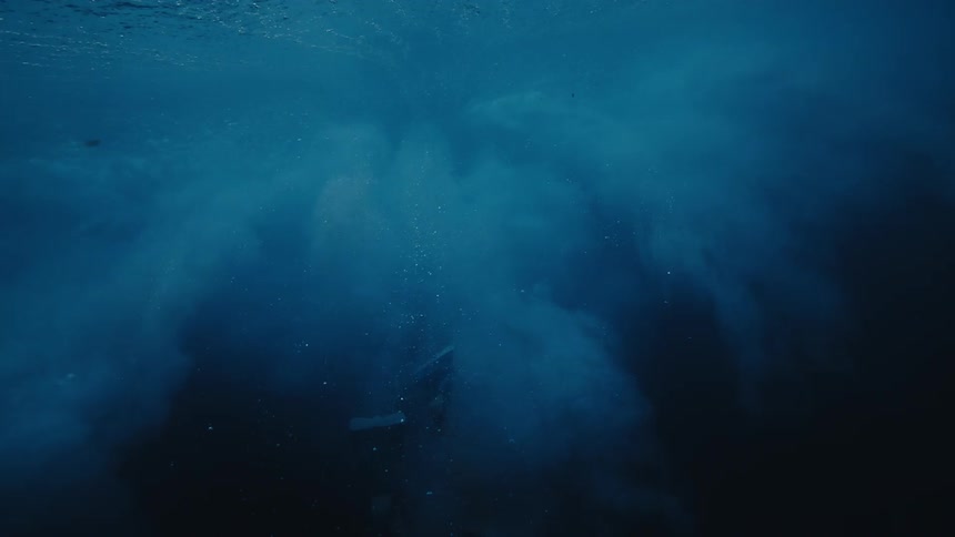 Swimmer swimming underwater swims toward the surface after wave crashes
