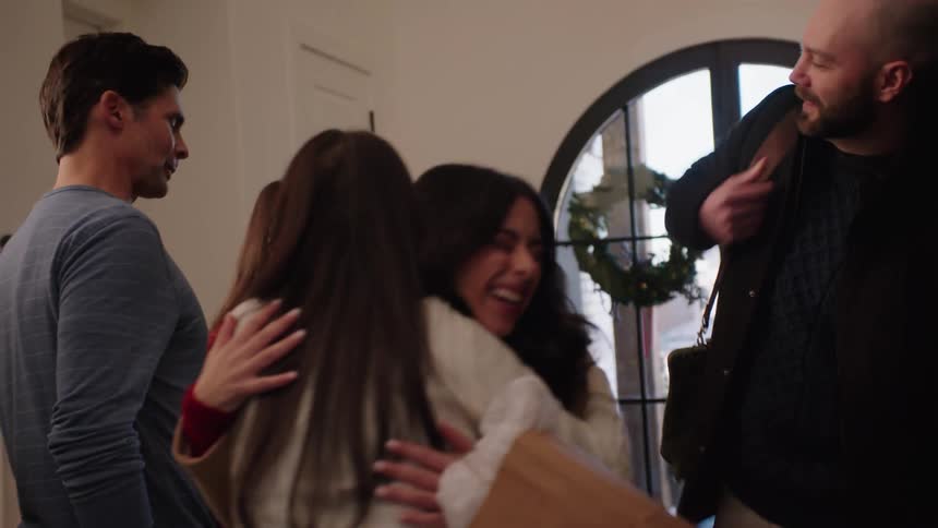 Man and woman holding gifts being greeted by another man woman and children hugging and smiling indoor