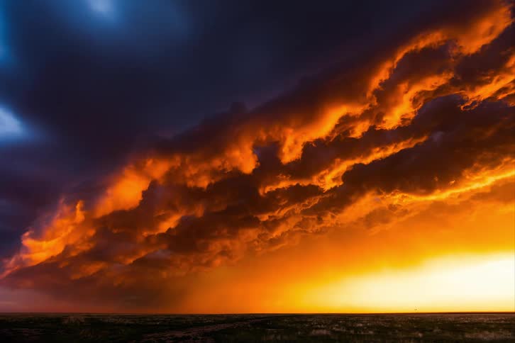Storm clouds move across the sky as the sun shines on the horizon reflecting on the clouds as lightning flashes