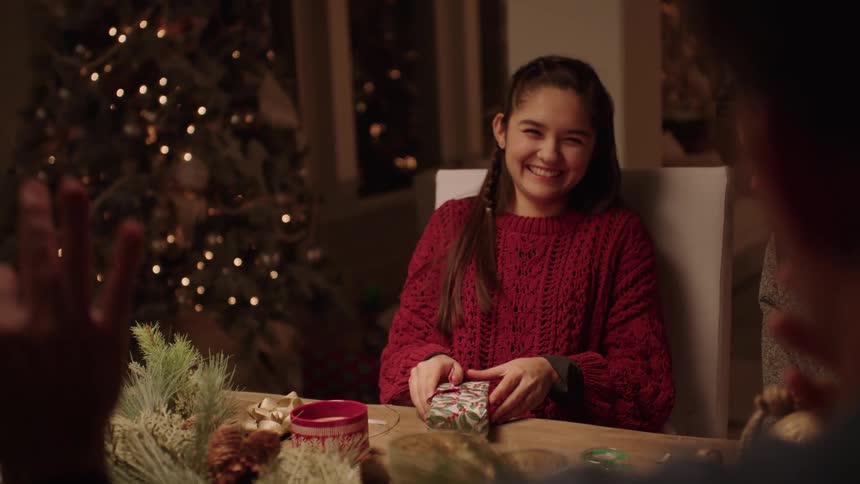 A clip of a a group of friends on a table having a conversation while a lady is wrapping a gift box