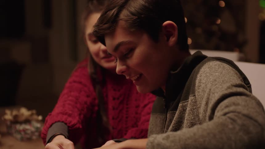Siblings wrapping christmas presents at a table