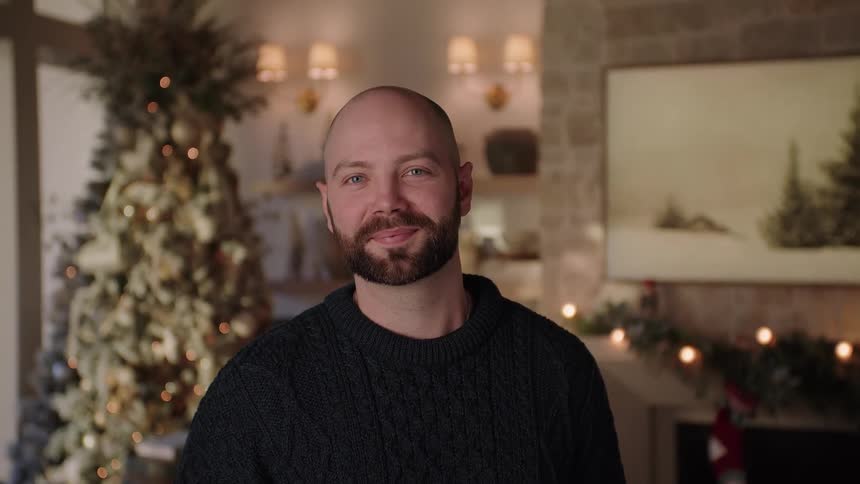 A bald bearded man standing in the living room at christmas looks at the camera