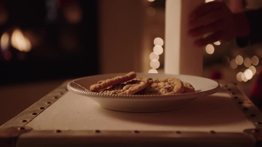 A person places a plate with cookies and a bottle of milk on a table and behind it there are many lights