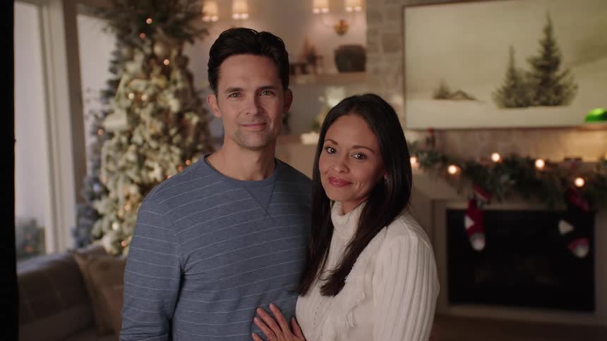 A couple standing together in a living room that is decorated for christmas