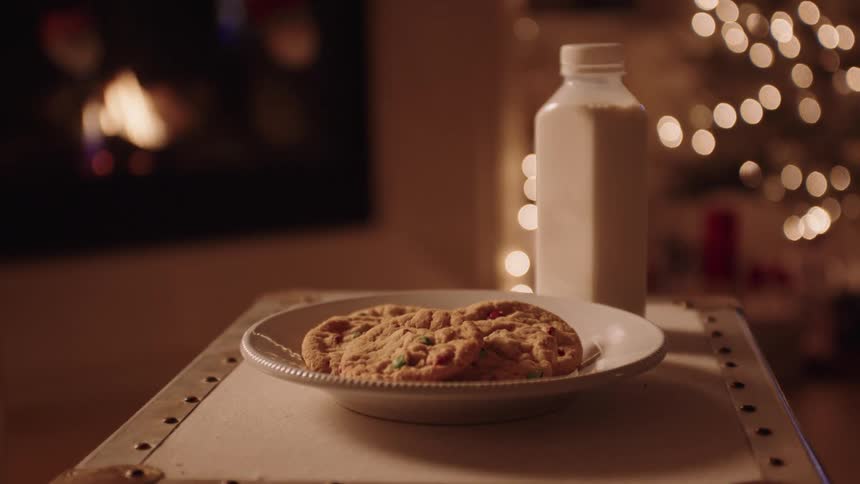A bottle of milk and cookies sits out at night in room with a christmas tree