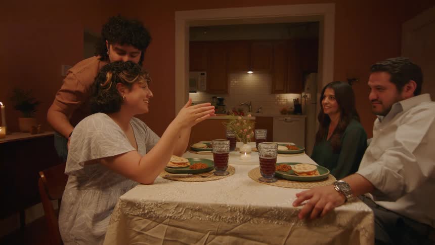 A man places a plate on a table where three other people sit and they all talk