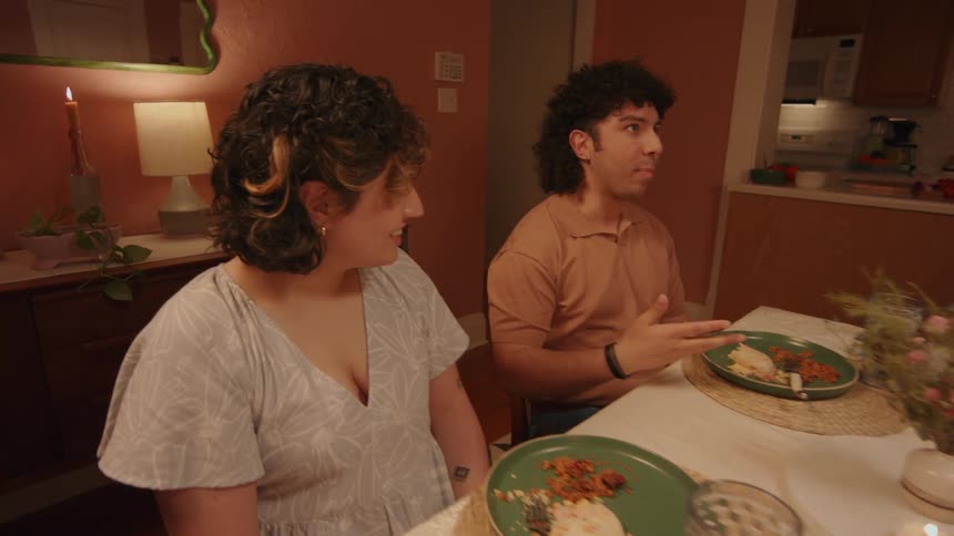 A man and a woman sit at a dining room table laughing and talking