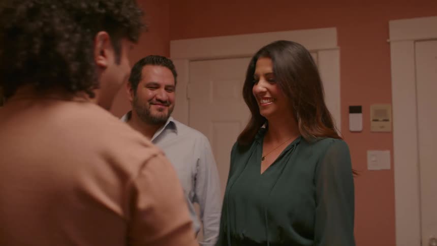 Three friends in a kitchen greet each other with hugs