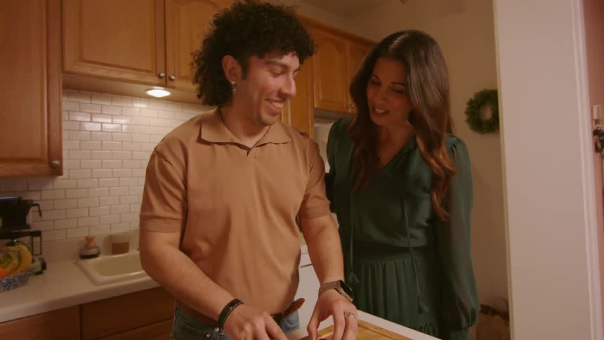 A man cutting tomatoes in the kitchen talks to his mom