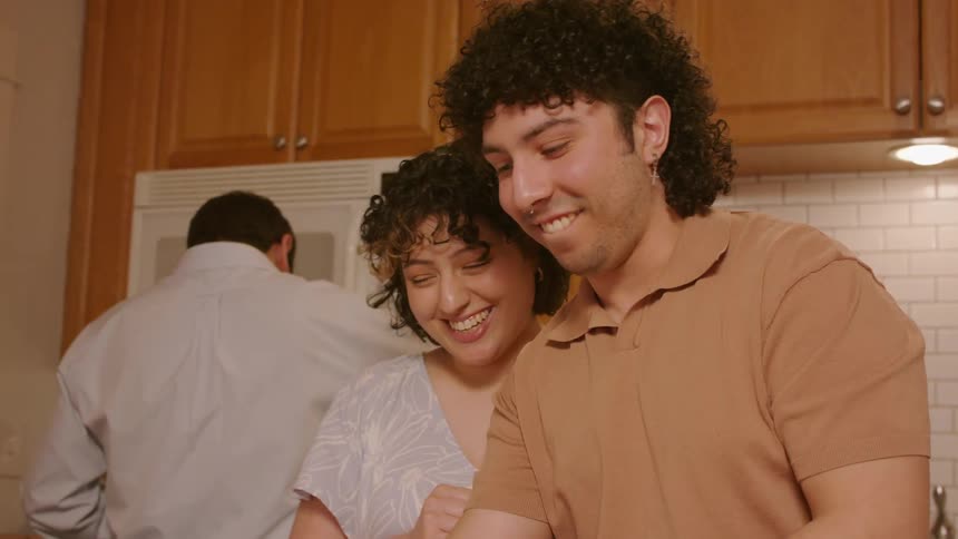Two young people cook in the kitchen together while talking and laughing
