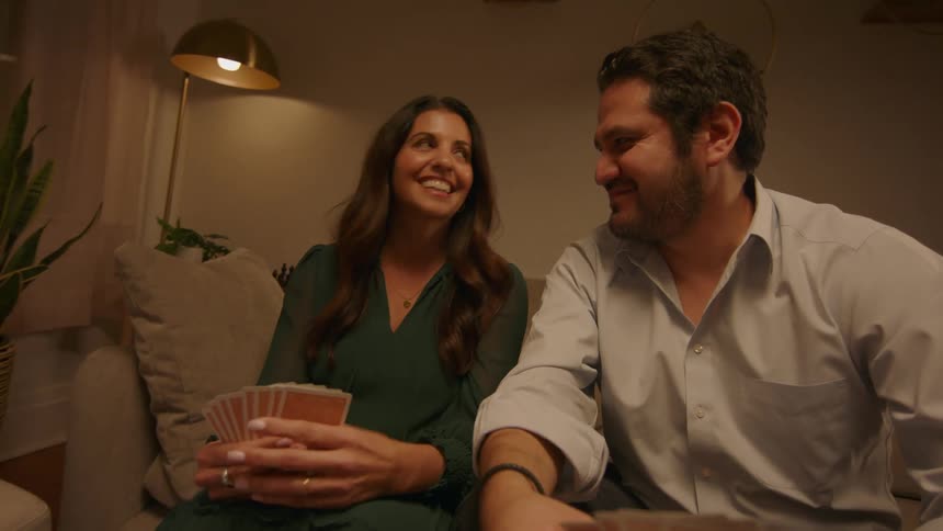 Two couples sitting in a living room talking laughing and playing cards