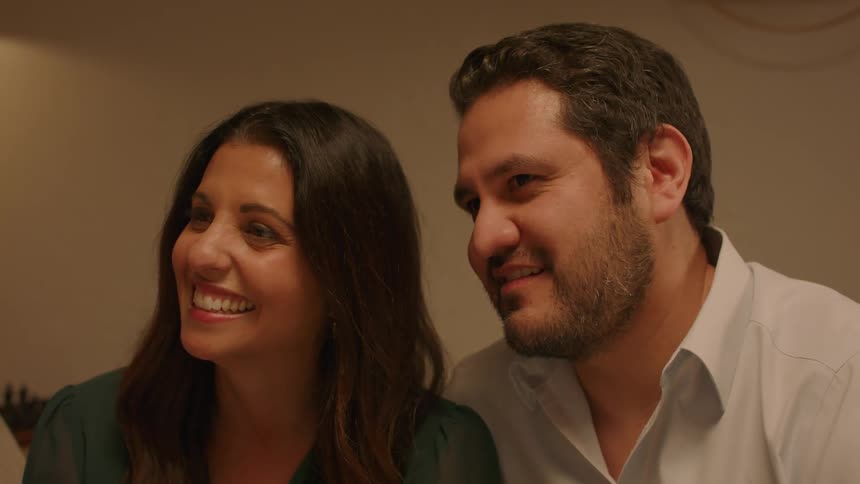 Couple sitting on couch cuddles together and smiles while talking