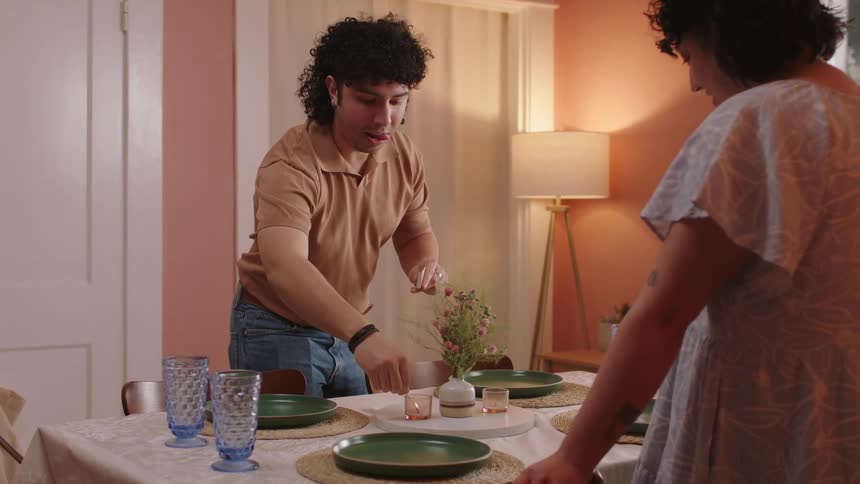 A standing man is lighting candles using a match and then gives an okay sign to a woman in front of him