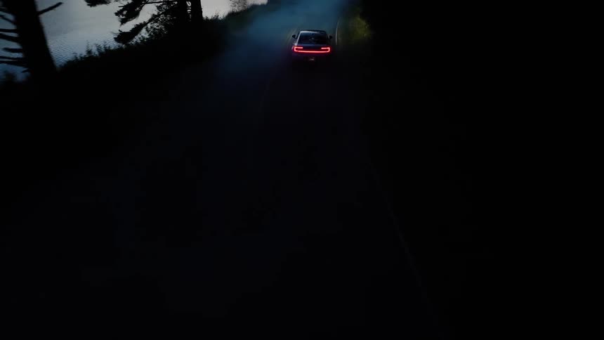 Aerial view of a car driving on a foggy road near a river