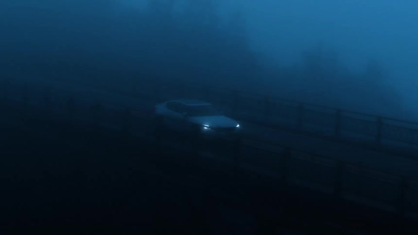 A car driving along a cloudy forest bridge road at night
