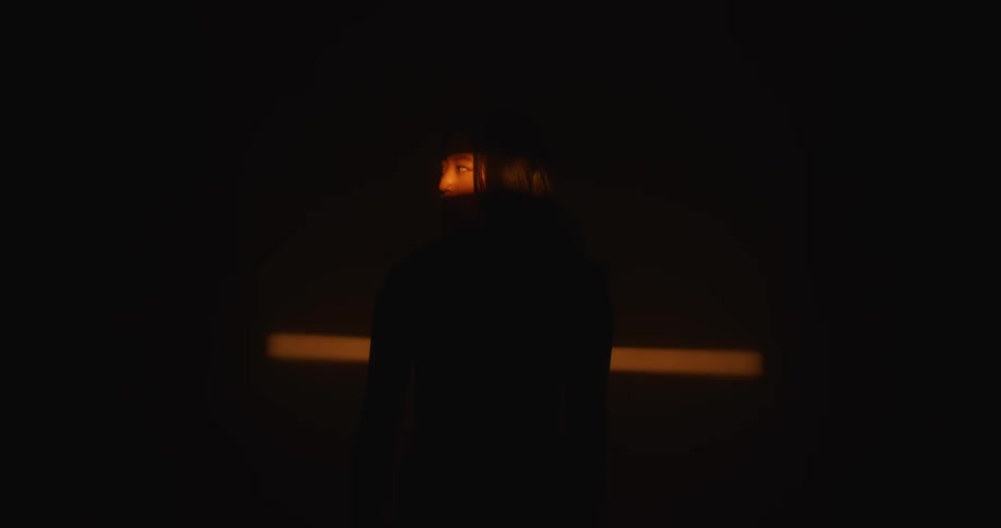 An asian woman stands in a light that illuminates her eyes and nose