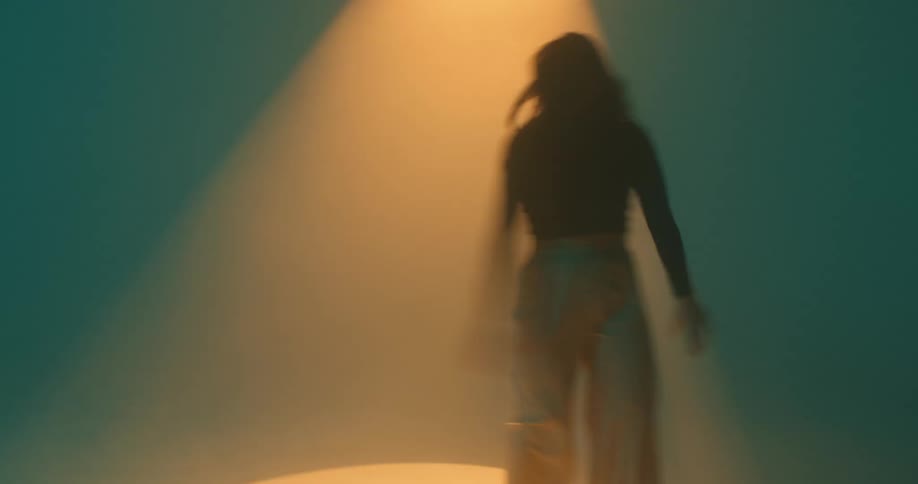 A woman dancing agressively under an orange spotlight