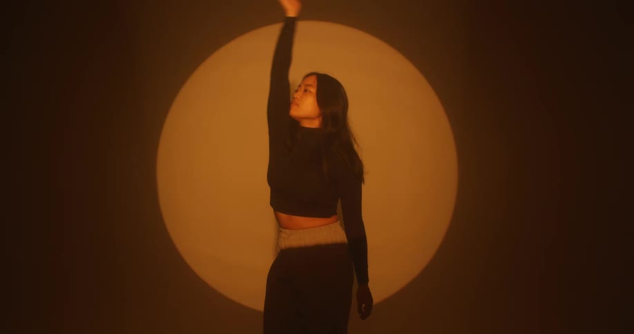 An asian woman dances in a spotlight