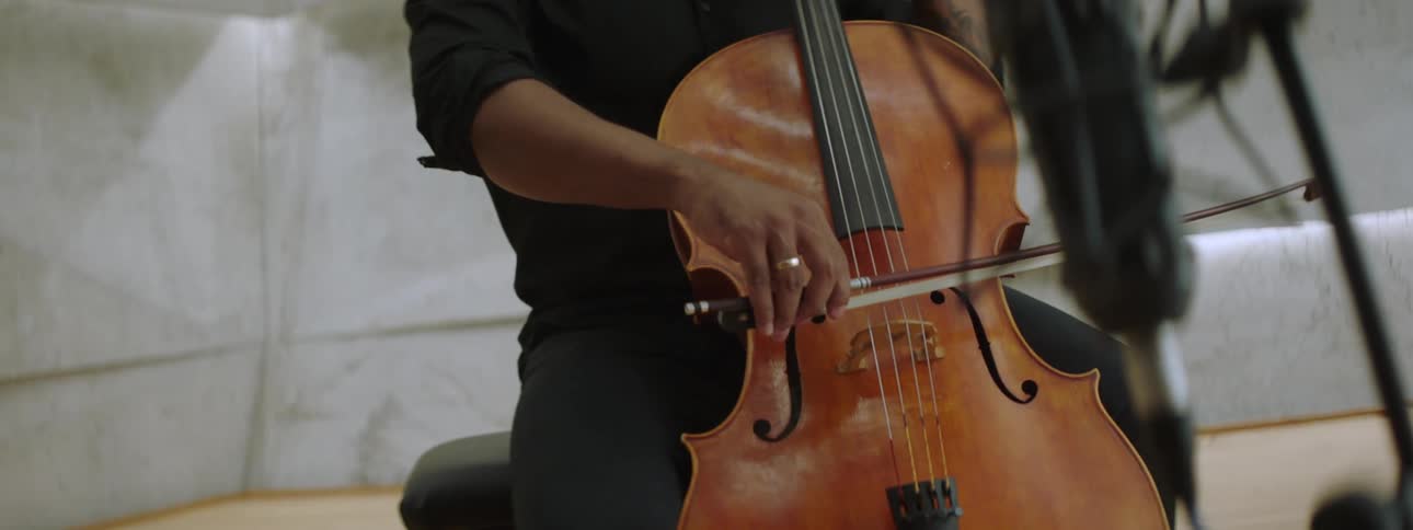 A man is sitting and playing a cello with a stick