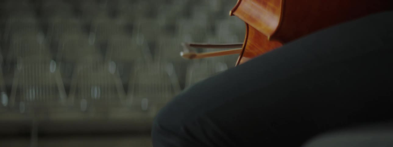 A person on stage playing the cello to an empty theatre