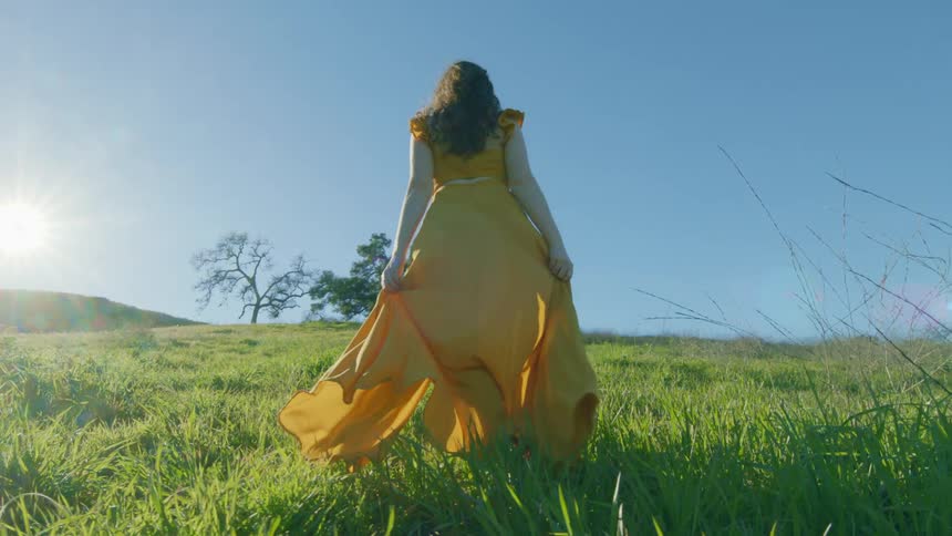Lady in yellow dress walking on grass on a sunny day