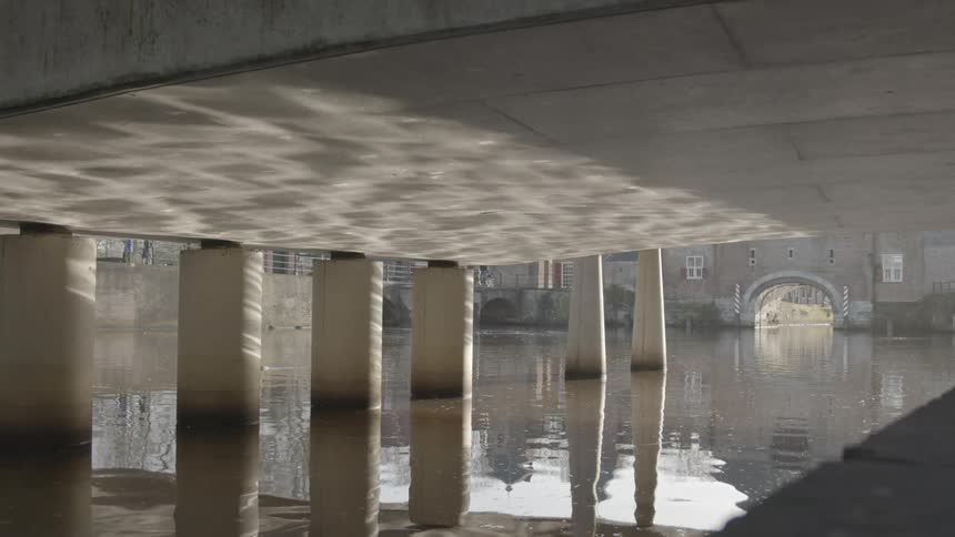 The water of a lake under a bridge is reflecting the surface on the bridge itself