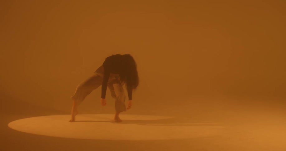 A woman dancing in a completely empty orange hazy room