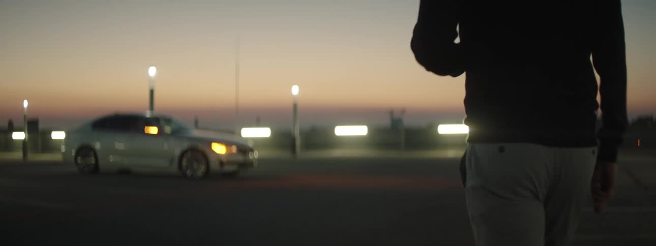 A man walking toward his parked motor vehicle at sunrise