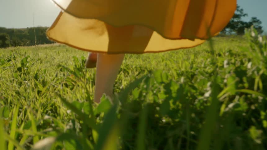A woman in a yellow dress walk on a green grass field on a sunny day