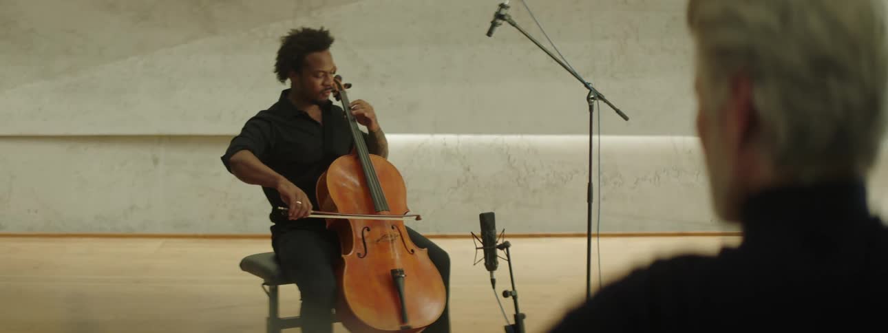 Man in a studio playing the violin and another person enjoying