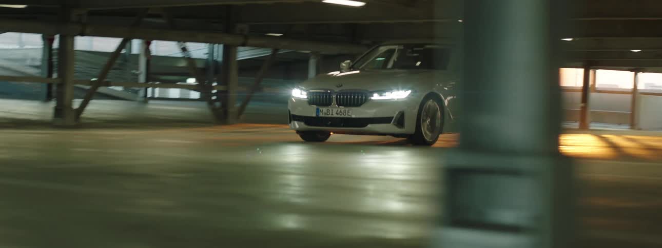 White bmw with illuminated headlights turning the corner in a parking garage at sunset