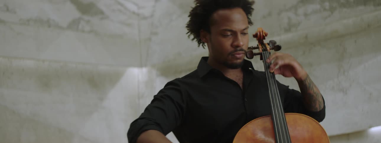 Male musician stands playing cello near a microphone