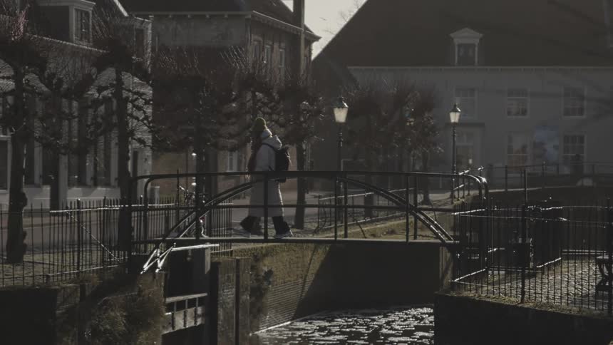A person walking on an iron bridge over a river in an urban region in winter