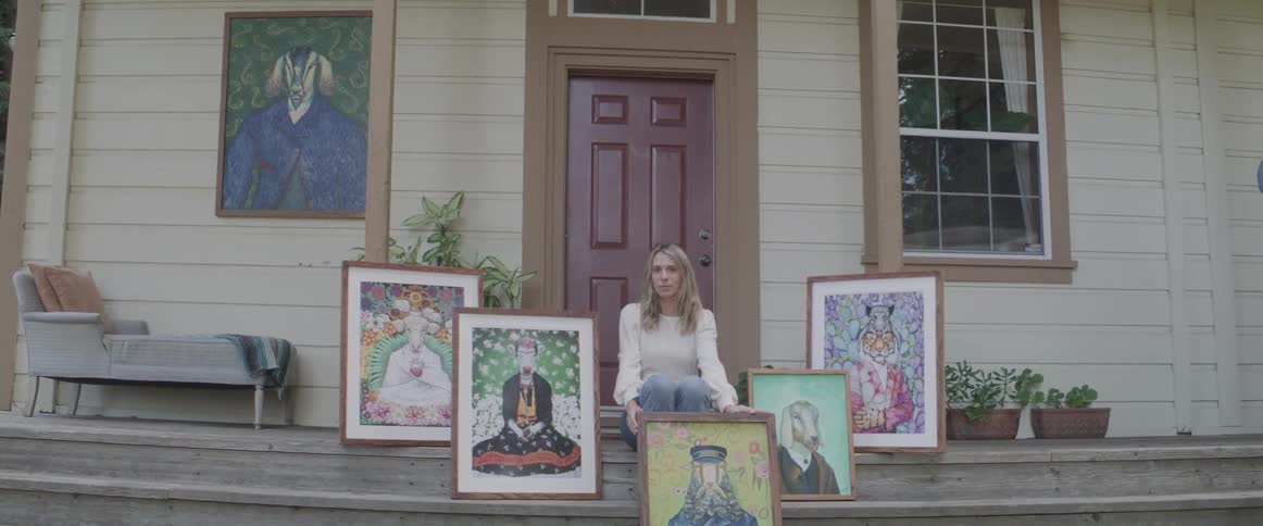 Blonde woman sits on steps in front of house with framed artwork