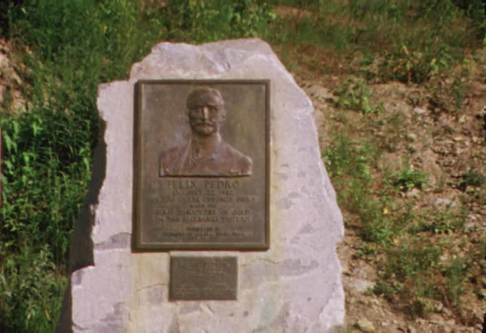 A monument affixed to a stone sits in a grassy field