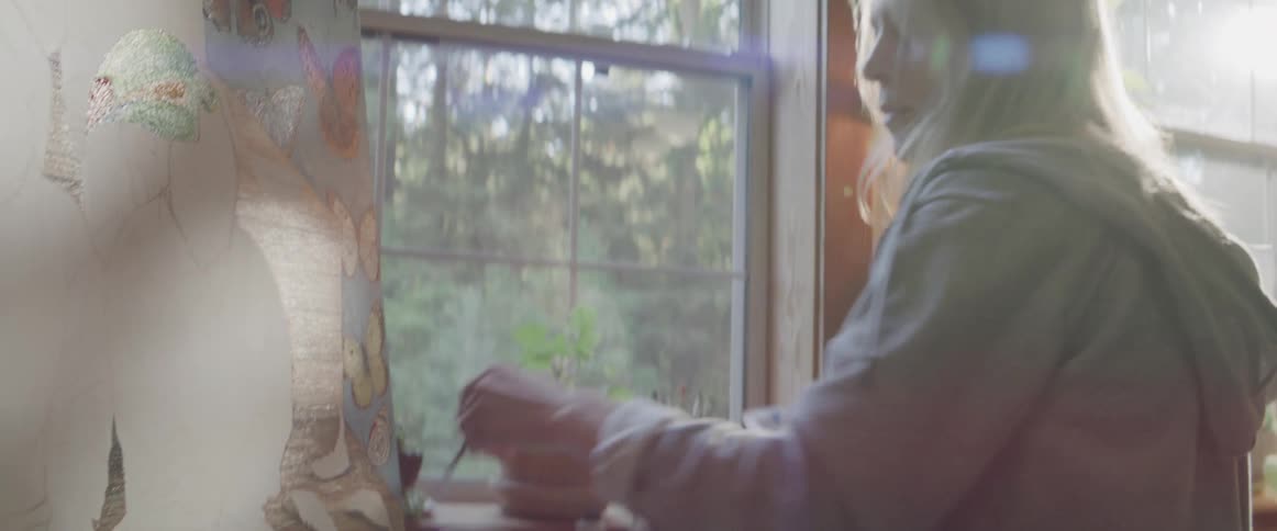 Blonde woman paints on canvas near window indoors