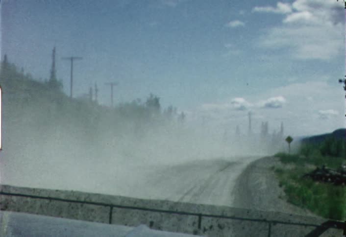 A truck is kicking up dust on a dirt road during the day
