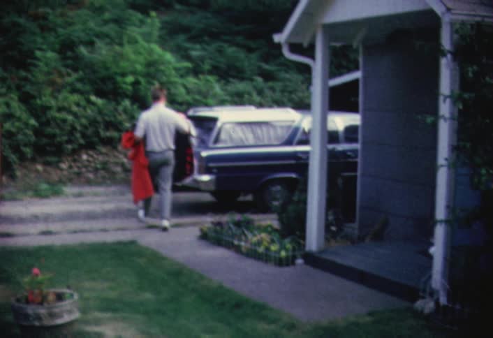 A man carries clothes out to a station wagon car