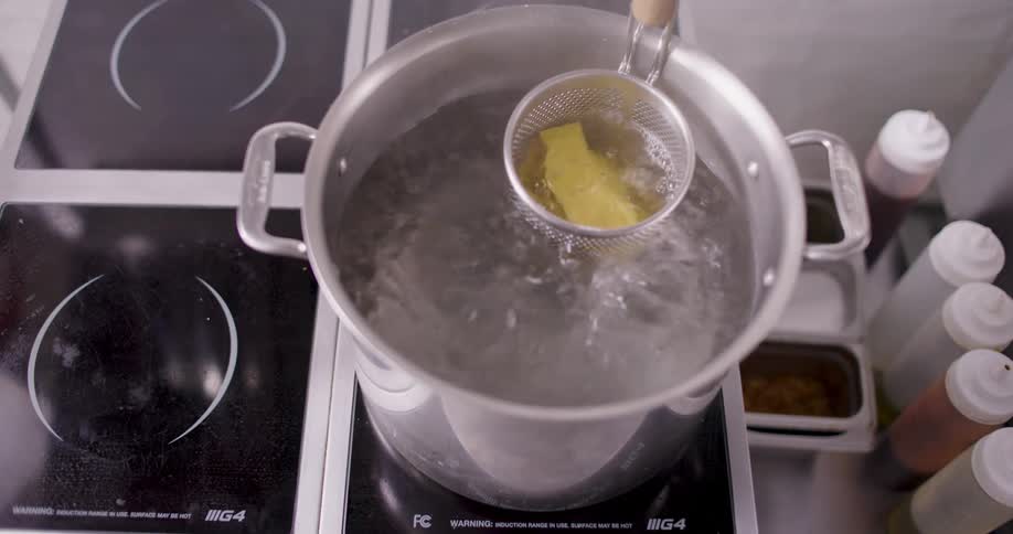 Am person places several flat pieces of pasta into a sieve in a pot of boiling water