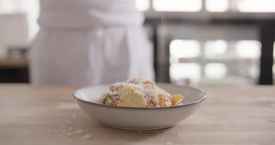 A bowl of pasta sitting on a cutting board has shredded cheese sprinkled atop it
