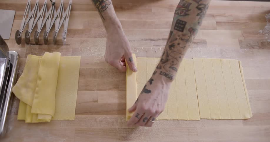 A person with many tattoos on their arms prepares some pasta from scratch