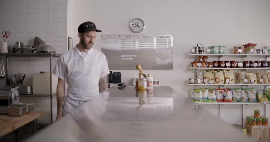 A man in white clothes hands a bag to a person behind a counter and they shake hands and that person leaves