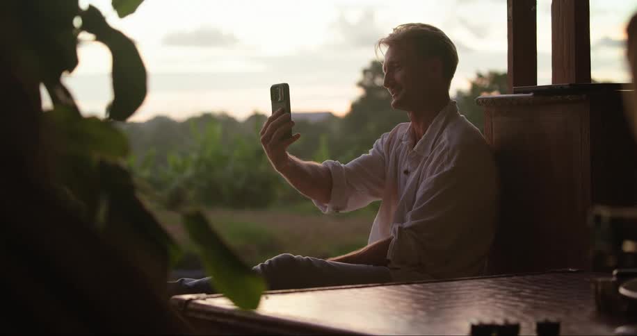A person sitting in the patio holding up a phone at evening