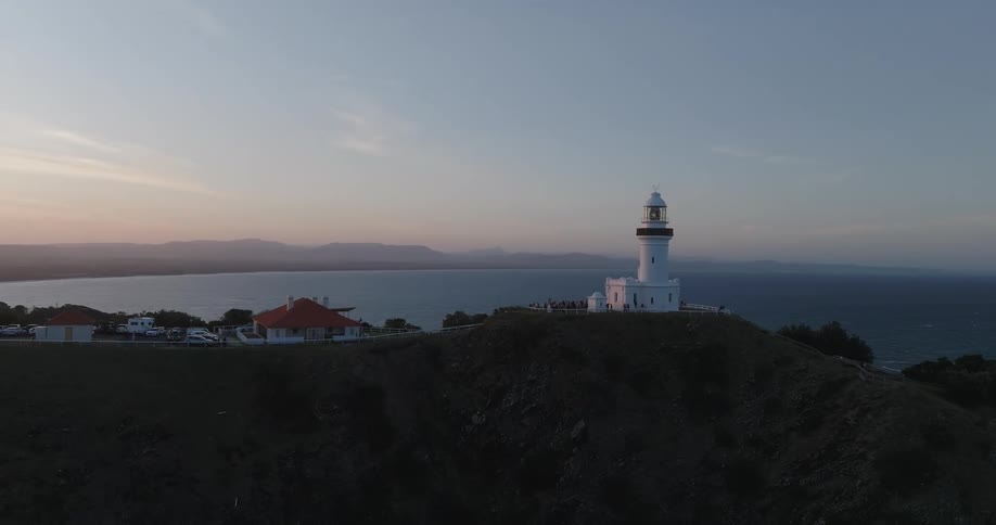 White lighthouse on a coastal cliff overlooking the ocean as the sunsets in the distance