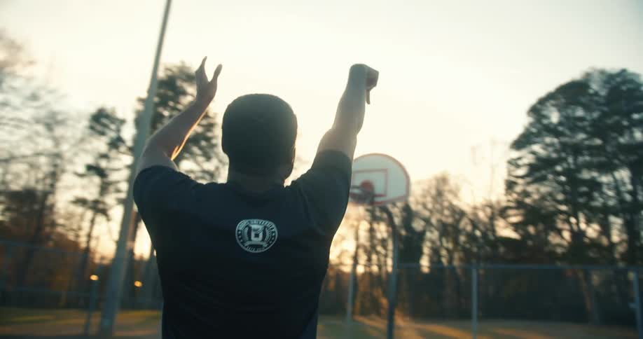 A man playing basketball outdoors at sunset