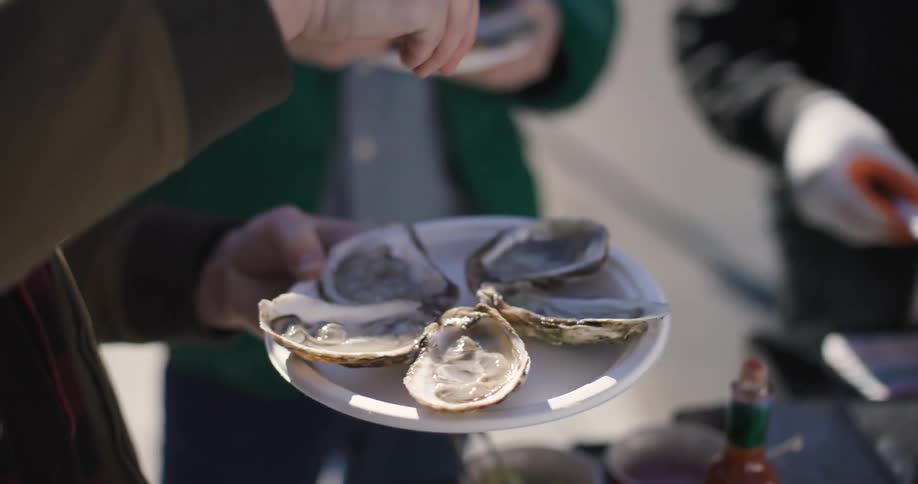 A person sprays lemon juice over a plate of oysters