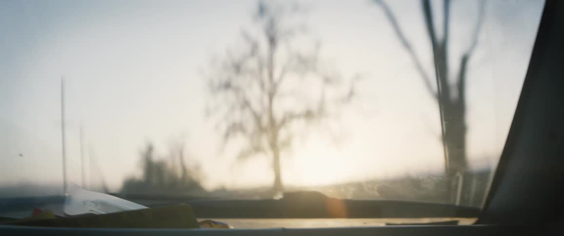 Vehicle drives along road though countryside as sun sets