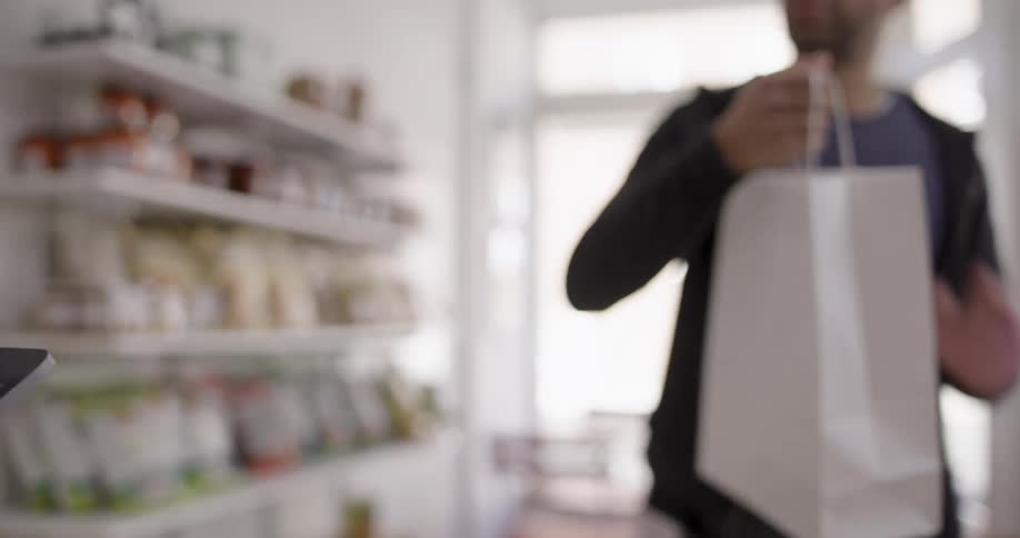 Worker shake hands with a male customer in a retail shop at midday while the customer took the shopping bag and walked away